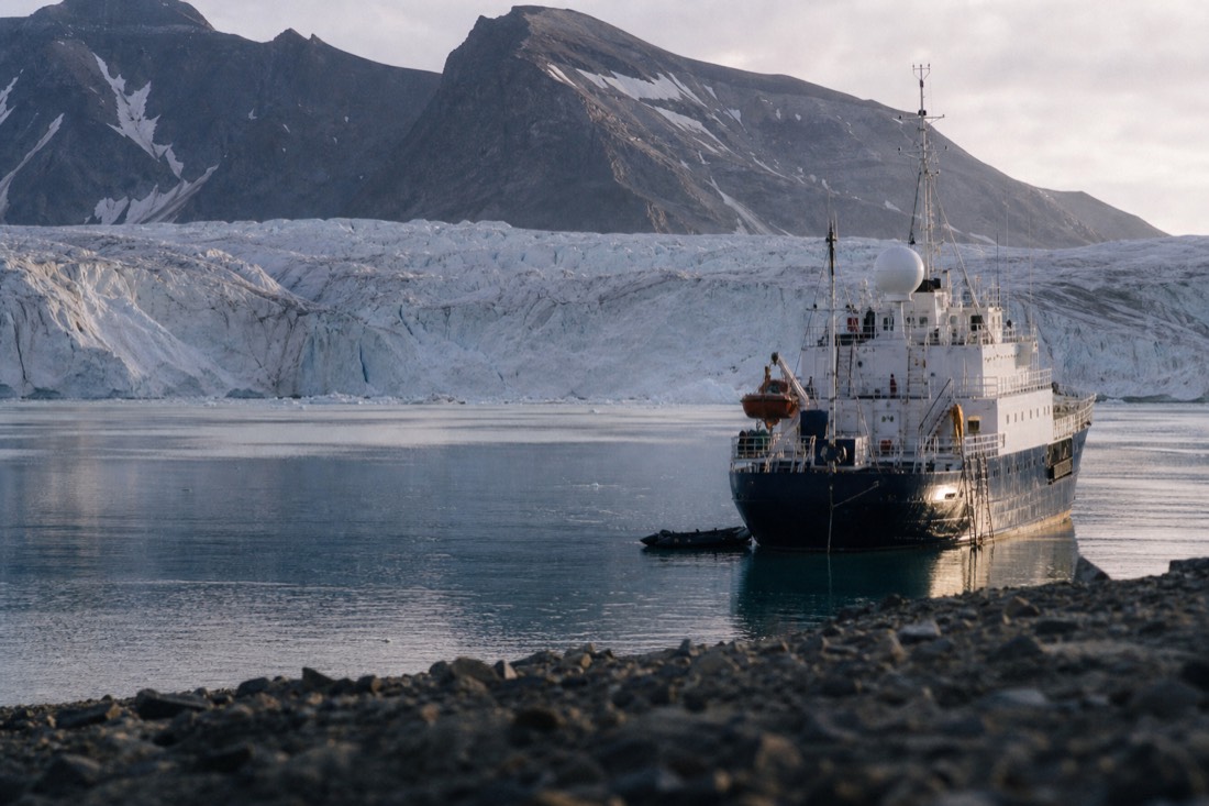 Small ice-strengthened expedition ship anchored in a remote Svalbard fjord below a glacier front
