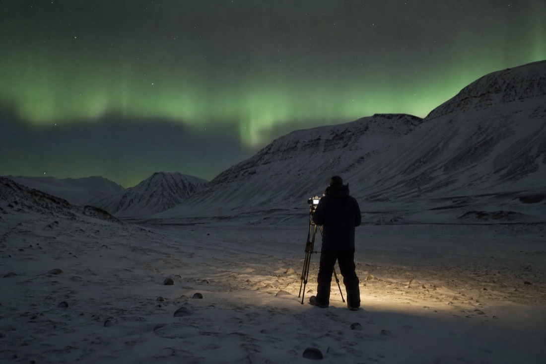 A photographer at a tripod under green aurora in Adventdalen on a Svalbard northern lights tour